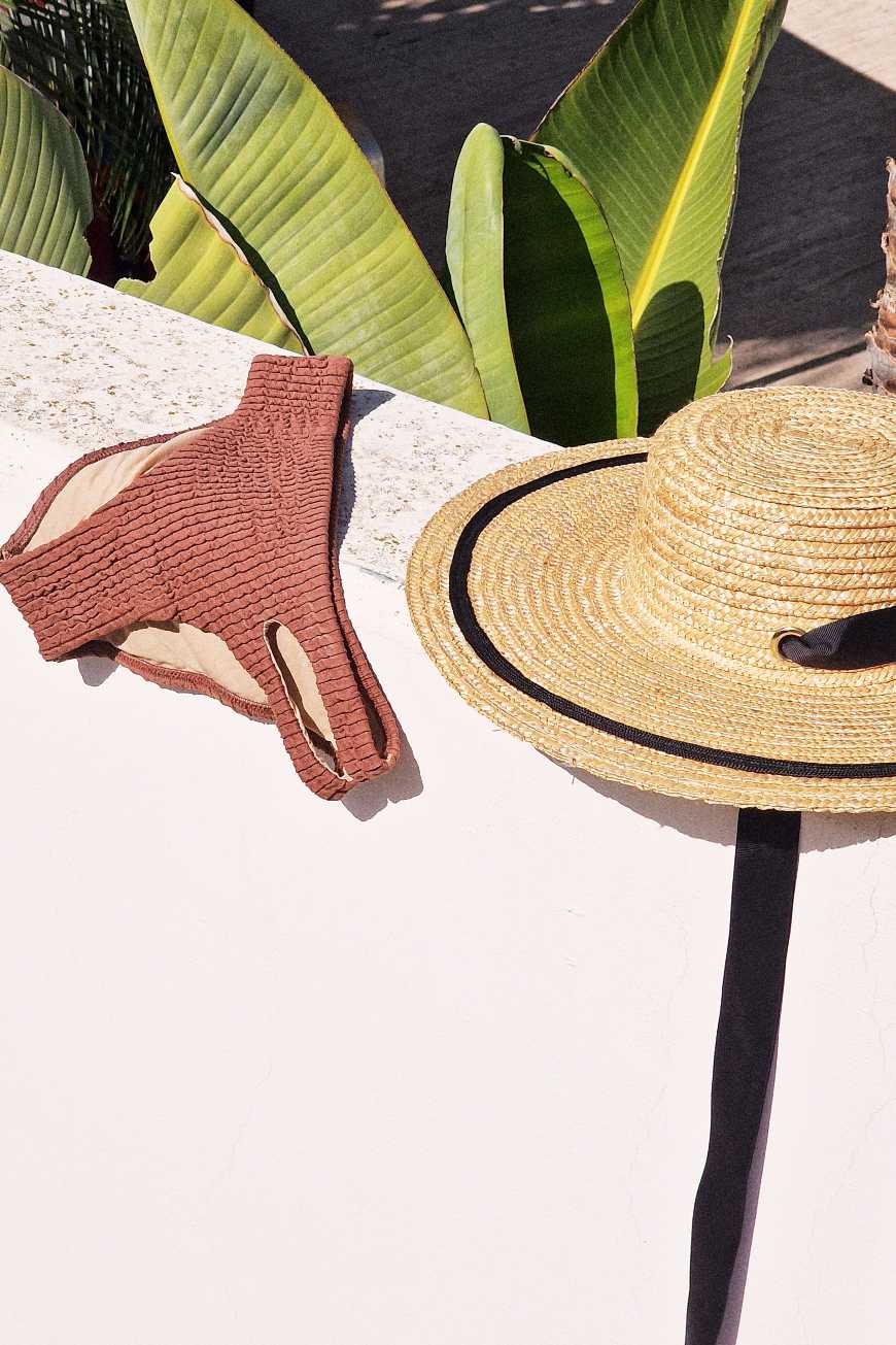 Kupaći kostim i slameni šešir na betonu pored biljke
