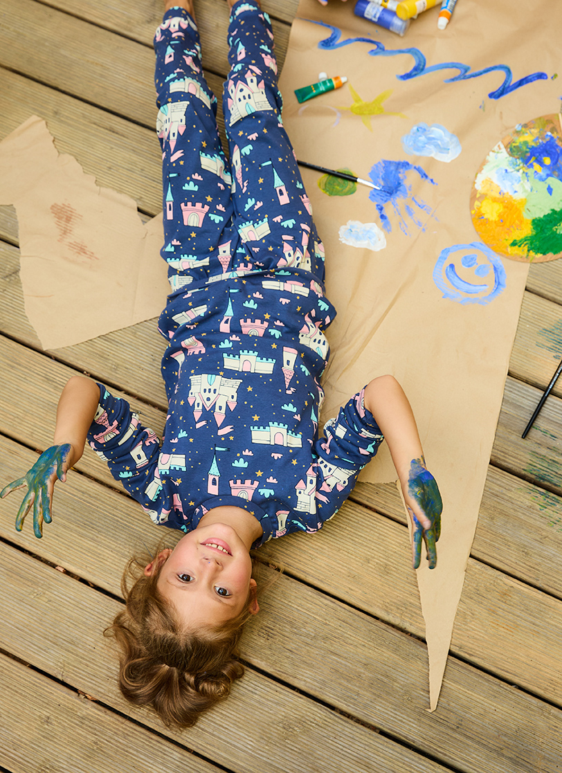 Devojčica leži napolju u plavoj pidžami na dug rukav i rukama obojenim temperama