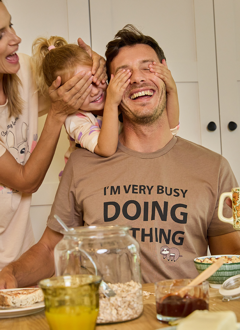 Nasmejan muškac sedi za stolom sa porodicom u braon pižama sa  motivom lenjivca