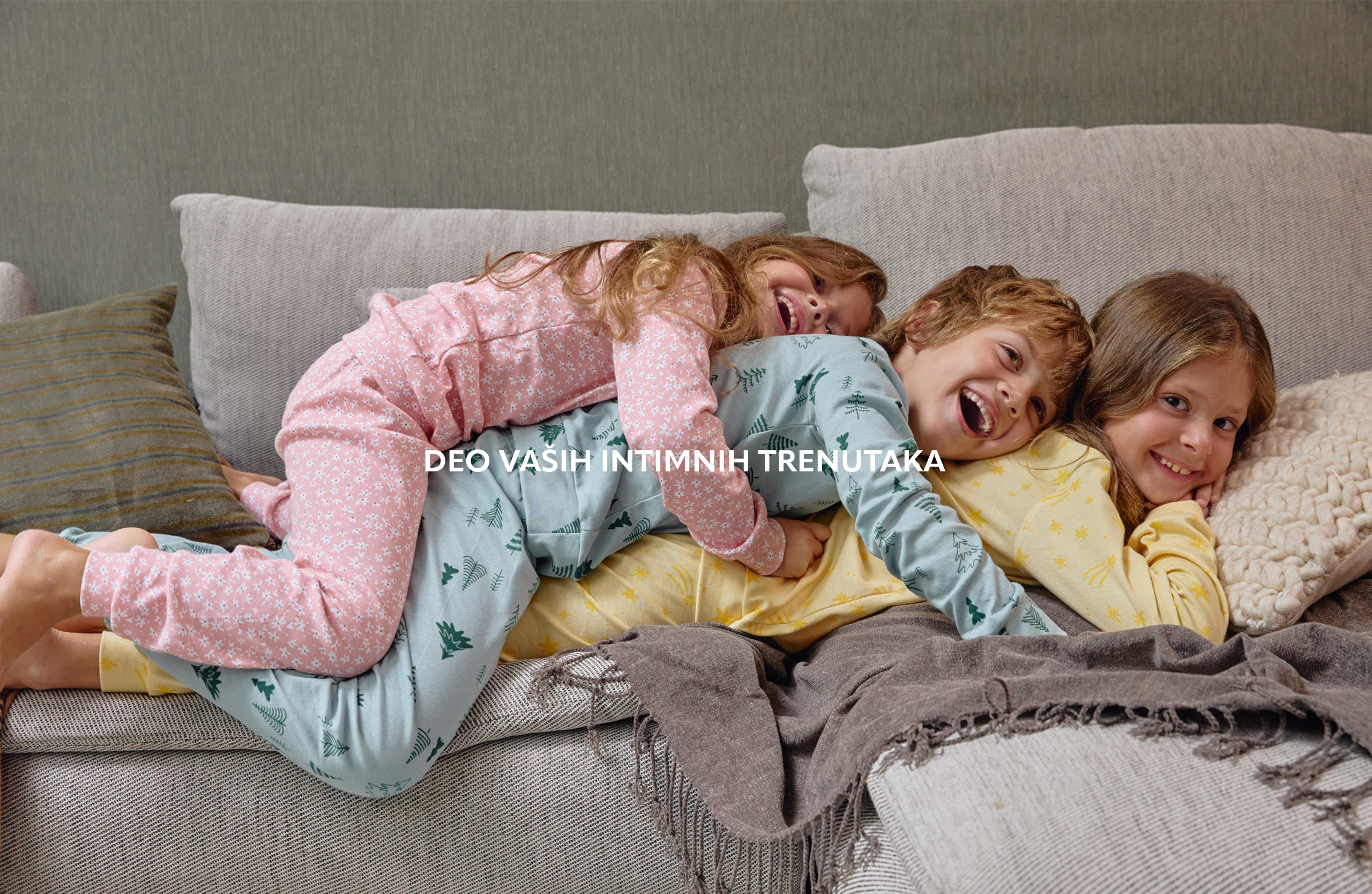 Dečak i dve devojčice leze na krevetu u šarenim pidžamama na dug rukav