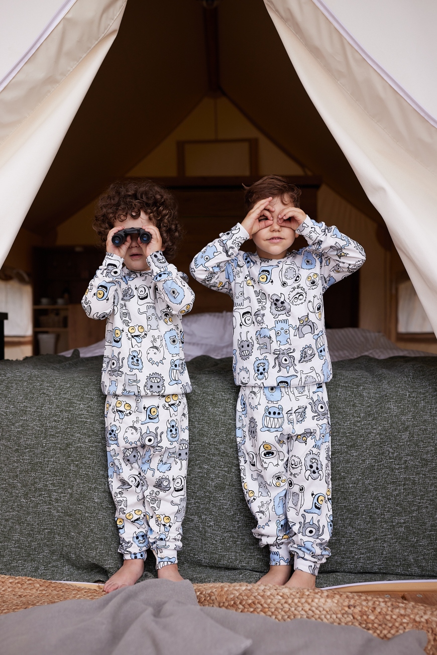 Dva dečaka u belim pidžamama sa dezenom čudovišta stoje ispred šatora i drže dvogled
