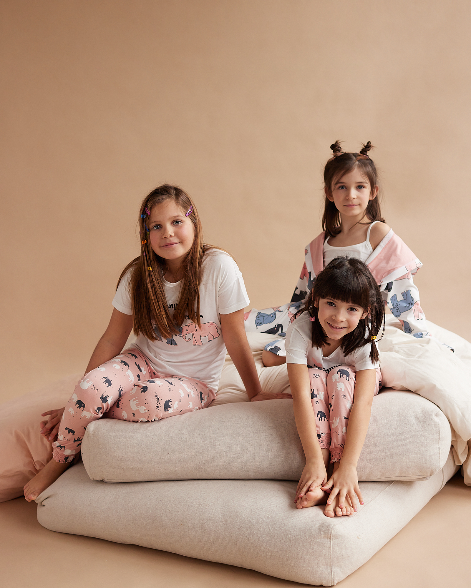 Tri devojčice u bež-roze pidžamama na kratak rukav sa motivom slonova sede na jstuku