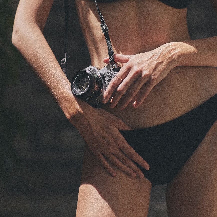 Devojka stoji u u crnom dvodelnom kupaćem i sa fotoaparaom u rukama