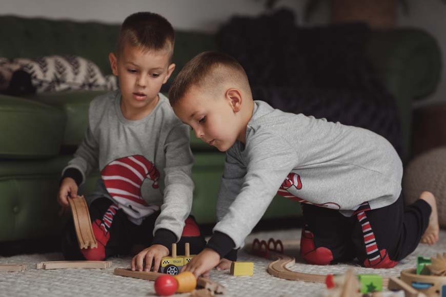 Dva dečaka u istoj odevnoj kombinaciji u sobi se igraju na podu