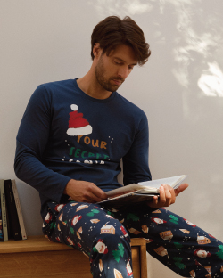 Muškarac u novogodišnjoj  pidžami na dug rukavi sedi i čita knjigu
