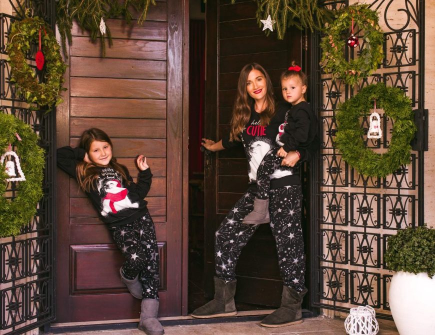 Žena sa dve devojčice stoji ispred vrata u crnim novogodišnjim pidžamama sa motivom foke