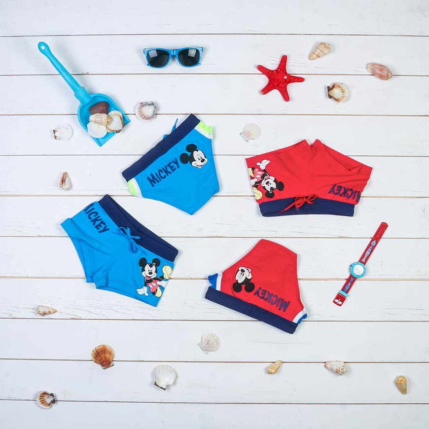 Plave i crvene gaće za dečake sa slikama Miki Mausa i pored njih se nalaze naočare za sunce, zvezda, lopata za plažu i sat