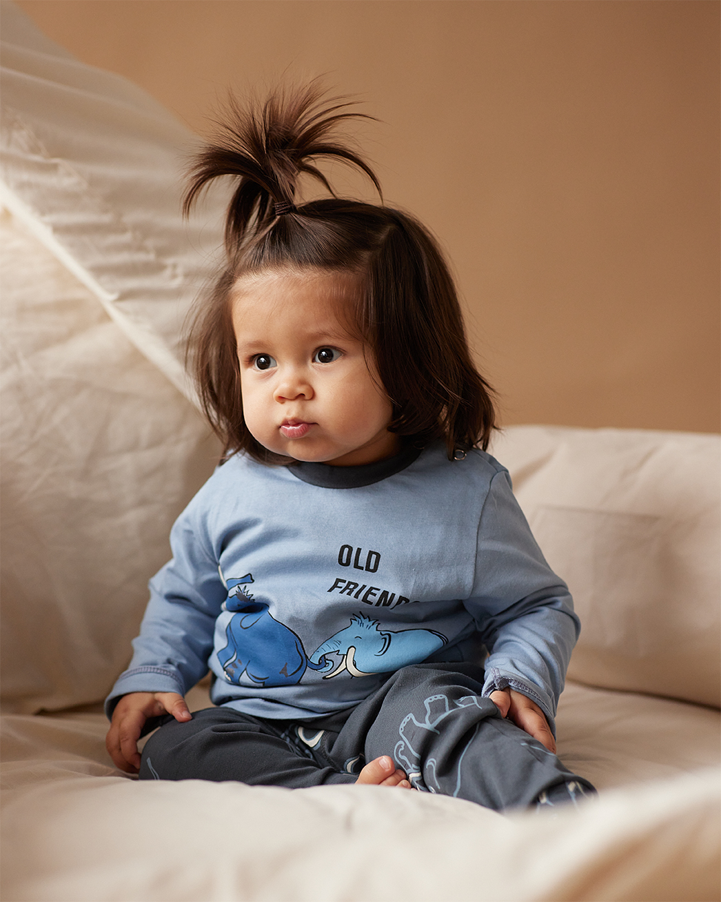 Dečak beba sedi na krevetu u plavoj pidžami na dug rukav sa motivom slonova